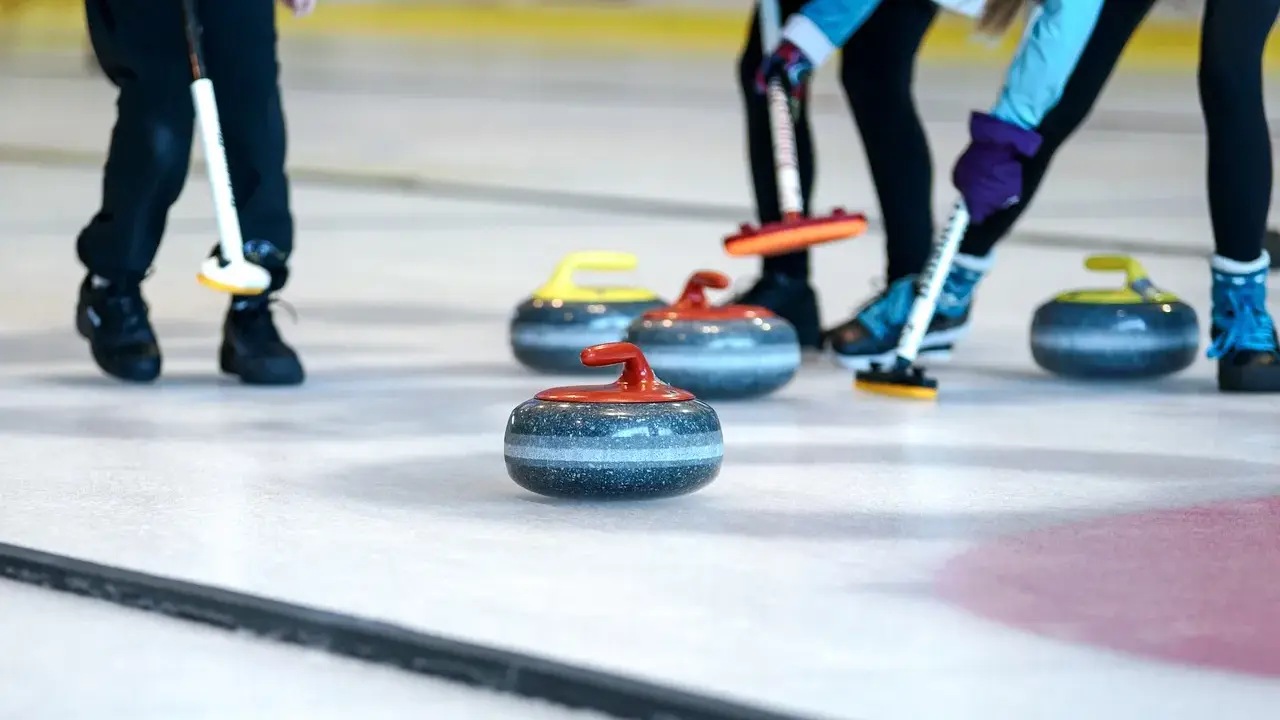 Curling ouders met hun stenen op het ijs. De spelers buigen zich voorover, klaar om te gooien.