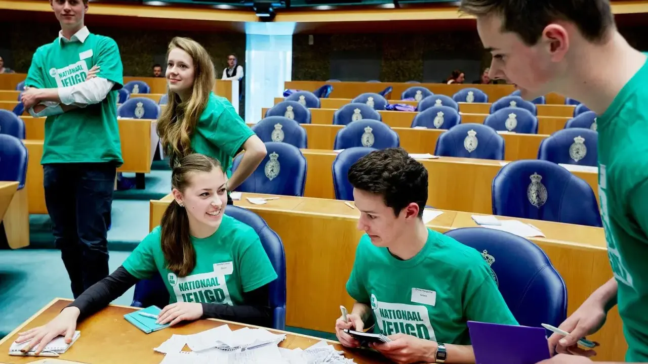 Jongeren in groene shirts met 'Nationaal Jeugdparlement' opdruk, discussiëren in de Tweede Kamer. Ze pleiten voor stemrecht naar 16 jaar.