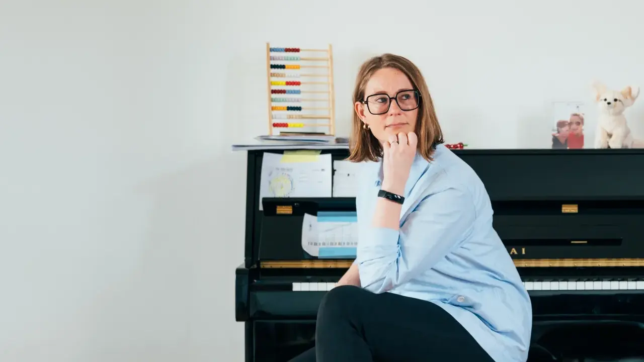 Annelien de Dijk, met een blik vol vrijheid, zit bij een piano, omringd door muziek en een telraam.