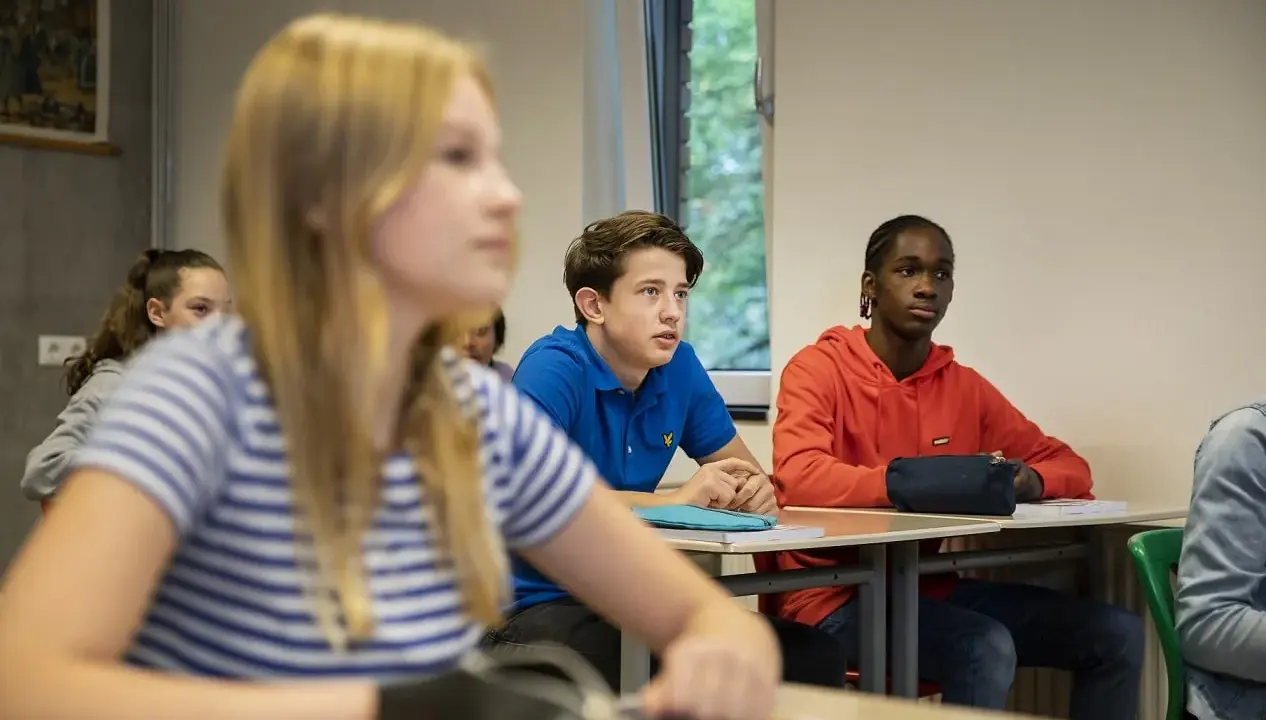 Leerlingen in een klaslokaal, met een jongen in een blauw shirt die aandachtig luistert. Dit beeld toont leuke manieren om je klas stil te krijgen.
