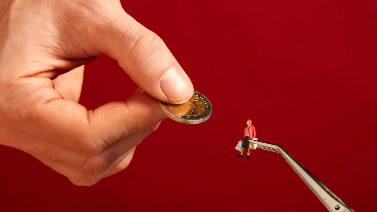 Een hand houdt een munt vast, terwijl een pincet een miniatuurfiguur met boodschappentassen vasthoudt. Dit symboliseert hoe een filantroop helpt.