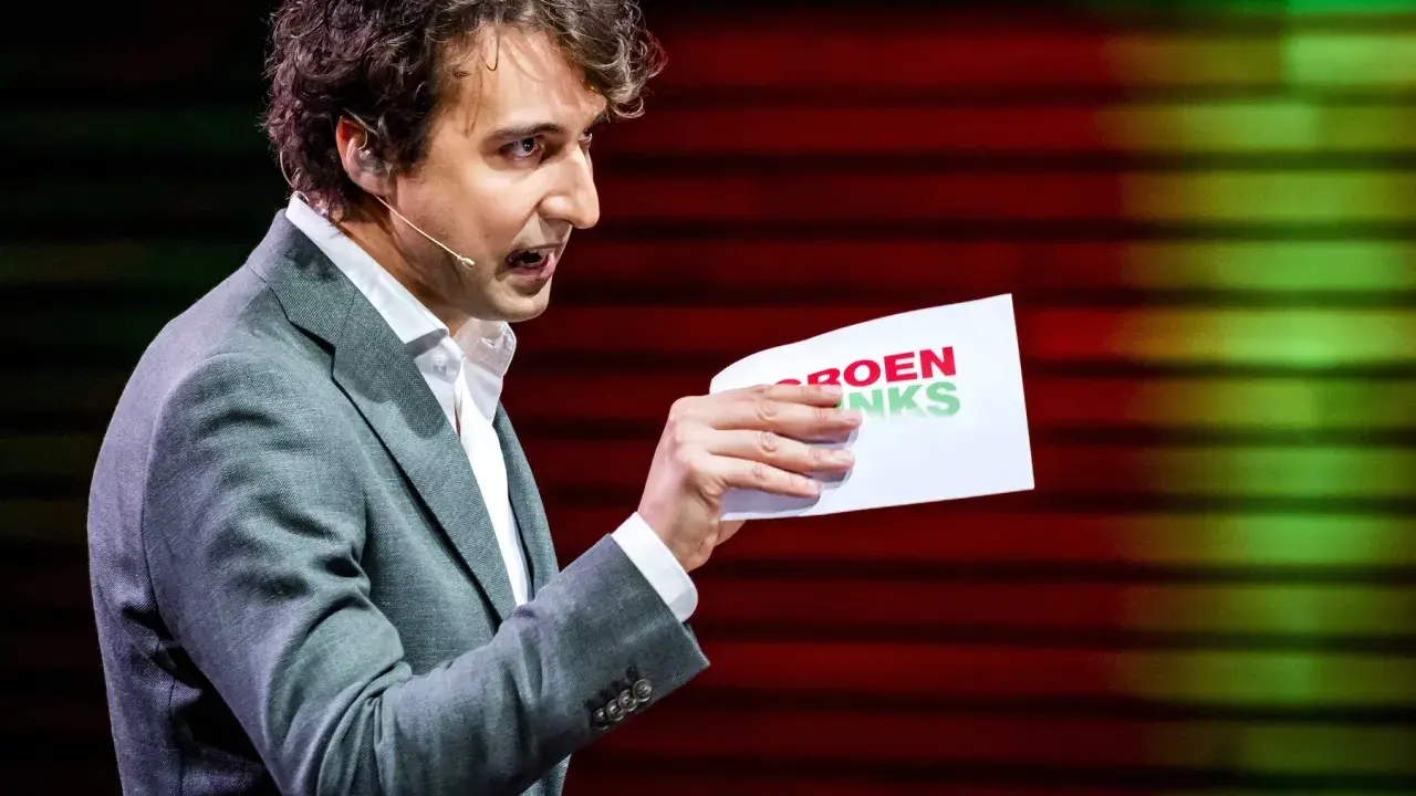 Man met krullend haar, in grijs pak, houdt een papier met "GROENLINKS" vast. Discussie over de Moslimbroederschap?