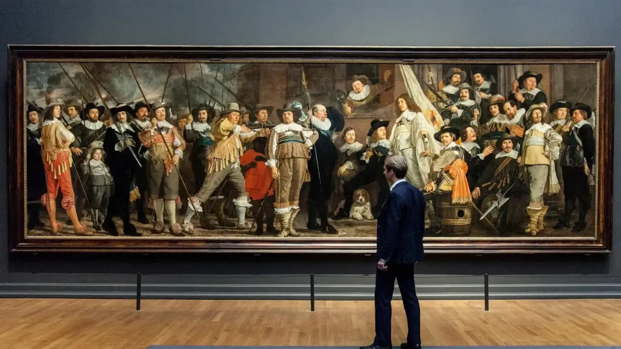Man kijkt naar De Nachtwacht, een schilderij dat de Nederlandse nationale identiteit weerspiegelt met zijn dynamische groepsportret van schutters.