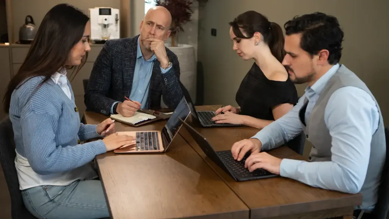 Teamoverleg: de betekenis van delegeren wordt duidelijk als de manager taken verdeelt en de teamleden geconcentreerd werken aan hun laptops.