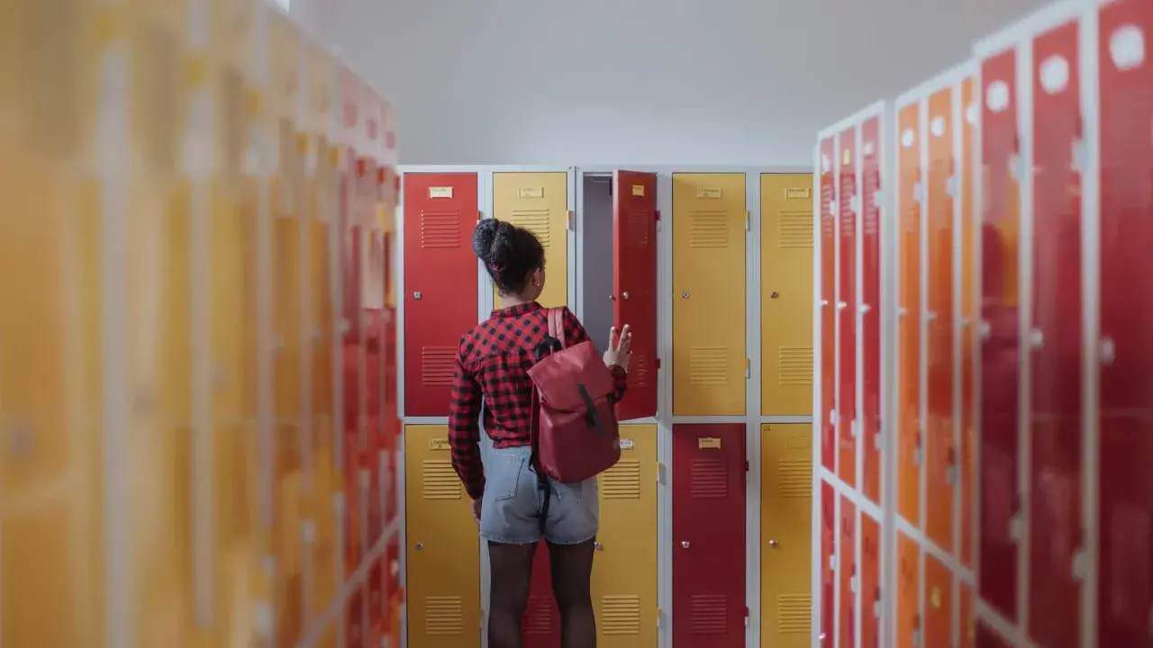 Meisje met rugzak bij schoolkluisjes. Ze overweegt of ze van 3 havo naar 4 mavo kan.