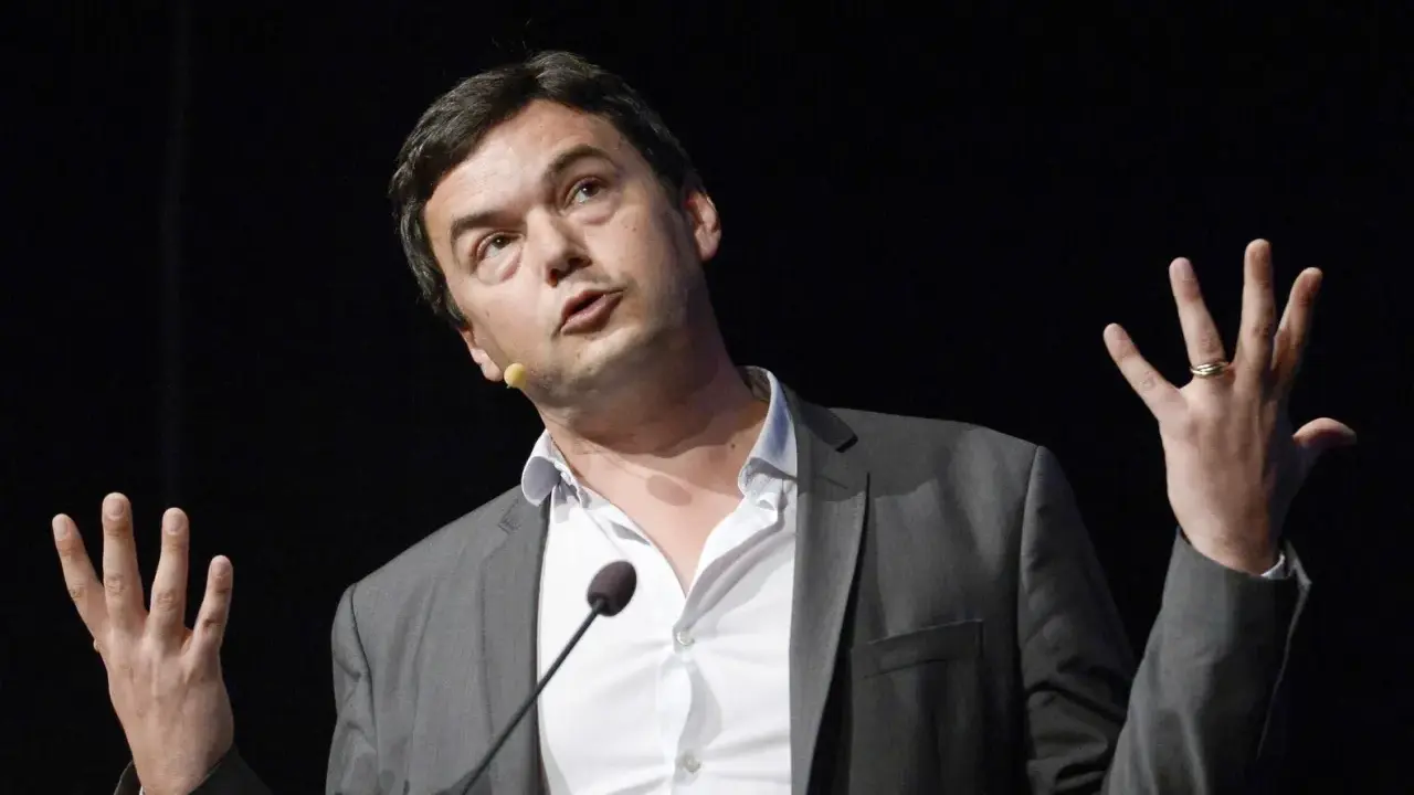 Economist Thomas Piketty spreekt met gebaren, zijn handen omhoog, terwijl hij een lezing geeft.