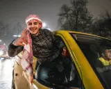 Jonge Marokkaanse Nederlanders vieren feest in een gele auto, met een van hen die uit het raam hangt en lachend zwaait.