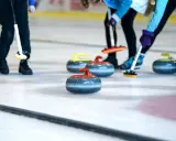 Curling ouders met hun stenen op het ijs. De spelers buigen zich voorover, klaar om te gooien.