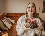 Vrolijke vrouw met bril en koptelefoon viert haar verjaardag met een chocoladetaart. Ze heeft de volwassen leeftijd bereikt en straalt van geluk.