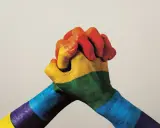 Twee handen, beschilderd met de regenboogkleuren, omstrengeld. Een symbool van verbondenheid en de strijd voor sociale rechtvaardigheid.