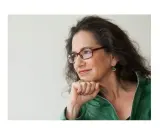 Susan Neiman, met een denkbeeldige blik, draagt een groene jas en een bril.