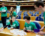 Jongeren in groene shirts met 'Nationaal Jeugdparlement' opdruk, discussiëren in de Tweede Kamer. Ze pleiten voor stemrecht naar 16 jaar.