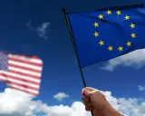 Hand holds EU flag, US flag blurred in background. Discussing what is soevereiniteit in a global context.