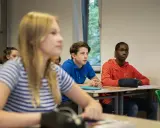 Leerlingen in een klaslokaal, met een jongen in een blauw shirt die aandachtig luistert. Dit beeld toont leuke manieren om je klas stil te krijgen.