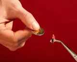 Een hand houdt een munt vast, terwijl een pincet een miniatuurfiguur met boodschappentassen vasthoudt. Dit symboliseert hoe een filantroop helpt.