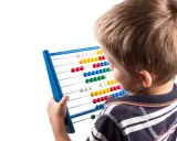 Jongen met telraam, leert getallen en patronen. Dit is een vorm van assimilatie en accommodatie in de ontwikkeling.