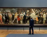 Man kijkt naar De Nachtwacht, een schilderij dat de Nederlandse nationale identiteit weerspiegelt met zijn dynamische groepsportret van schutters.