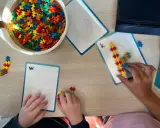 Kinderen bouwen met kleurrijke stukjes aan patronen op kaarten. Een mand vol bouwstenen ligt klaar voor meer taal spelletjes.