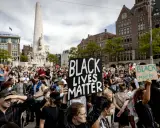 Mensen demonstreren op een plein met een monument, sommigen dragen borden met "Black Lives Matter".