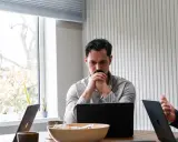 Man denkt diep na over beleid en maatschappij, omringd door laptops en plantjes.