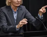 Vrouw in pak wijst met vinger, legt het gedachtegoed betekenis uit aan publiek.