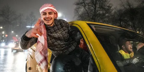 Jonge Marokkaanse Nederlanders vieren feest in een gele auto, met een van hen die uit het raam hangt en lachend zwaait.