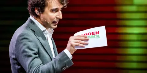 Man met krullend haar, in grijs pak, houdt een papier met "GROENLINKS" vast. Discussie over de Moslimbroederschap?