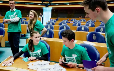 Jongeren in groene shirts met 'Nationaal Jeugdparlement' opdruk, discussiëren in de Tweede Kamer. Ze pleiten voor stemrecht naar 16 jaar.