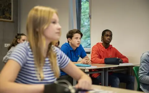Leerlingen in een klaslokaal, met een jongen in een blauw shirt die aandachtig luistert. Dit beeld toont leuke manieren om je klas stil te krijgen.