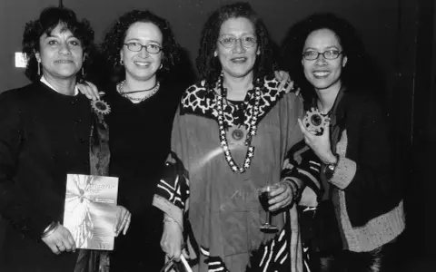 Vier vrouwen, symbool voor intersectionaliteit en feminisme, poseren met een boek en een glas wijn.