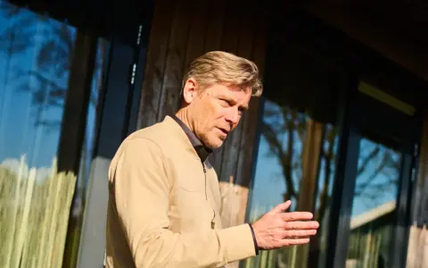 Man met blonde haren, gekleed in een beige jasje, legt met zijn hand uit hoe wordt ik assertiever.