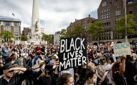 Mensen demonstreren op een plein met een monument, sommigen dragen borden met "Black Lives Matter".