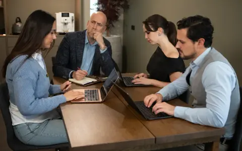 Teamoverleg: de betekenis van delegeren wordt duidelijk als de manager taken verdeelt en de teamleden geconcentreerd werken aan hun laptops.