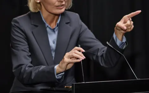 Vrouw in pak wijst met vinger, legt het gedachtegoed betekenis uit aan publiek.