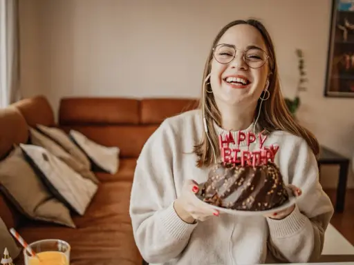 Vrolijke vrouw met bril en koptelefoon viert haar verjaardag met een chocoladetaart. Ze heeft de volwassen leeftijd bereikt en straalt van geluk.