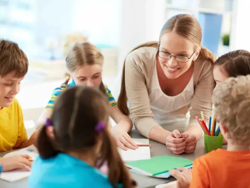 Docente begeleidt kinderen bij creatieve check-in werkvormen onderwijs. Kleurrijke potloden en notitieboekjes op tafel.