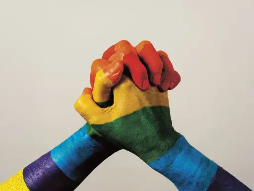 Twee handen, beschilderd met de regenboogkleuren, omstrengeld. Een symbool van verbondenheid en de strijd voor sociale rechtvaardigheid.