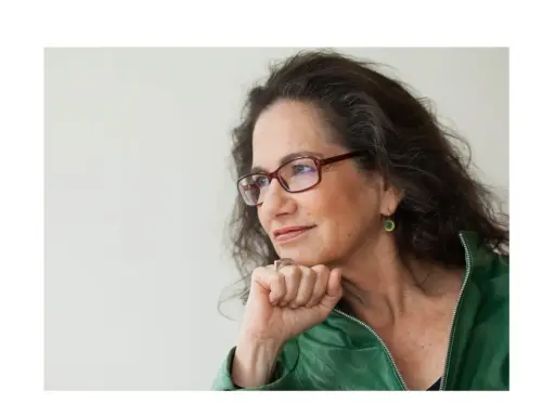 Susan Neiman, met een denkbeeldige blik, draagt een groene jas en een bril.