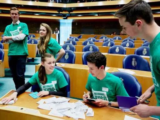 Jongeren in groene shirts met 'Nationaal Jeugdparlement' opdruk, discussiëren in de Tweede Kamer. Ze pleiten voor stemrecht naar 16 jaar.