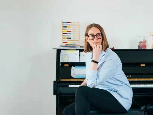 Annelien de Dijk, met een blik vol vrijheid, zit bij een piano, omringd door muziek en een telraam.