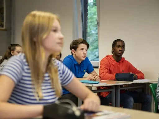 Leerlingen in een klaslokaal, met een jongen in een blauw shirt die aandachtig luistert. Dit beeld toont leuke manieren om je klas stil te krijgen.