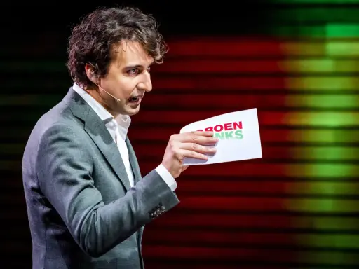 Man met krullend haar, in grijs pak, houdt een papier met "GROENLINKS" vast. Discussie over de Moslimbroederschap?