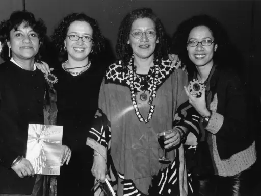 Vier vrouwen, symbool voor intersectionaliteit en feminisme, poseren met een boek en een glas wijn.