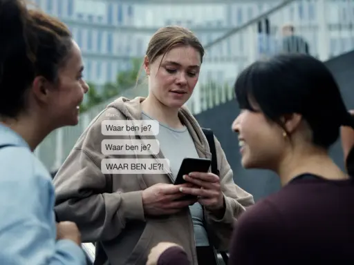 Drie vrouwen praten, één kijkt bezorgd naar haar telefoon met berichten als "Waar ben je?". Dit kan duiden op de angst die gepaard gaat met huiselijk geweld bij vrouwen.