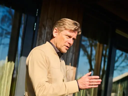 Man met blonde haren, gekleed in een beige jasje, legt met zijn hand uit hoe wordt ik assertiever.