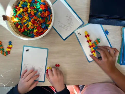 Kinderen bouwen met kleurrijke stukjes aan patronen op kaarten. Een mand vol bouwstenen ligt klaar voor meer taal spelletjes.