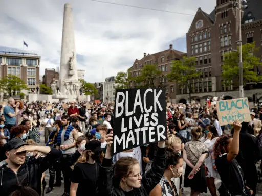 Mensen demonstreren op een plein met een monument, sommigen dragen borden met "Black Lives Matter".