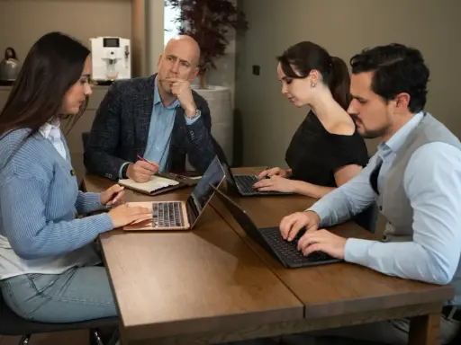 Teamoverleg: de betekenis van delegeren wordt duidelijk als de manager taken verdeelt en de teamleden geconcentreerd werken aan hun laptops.