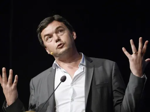 Economist Thomas Piketty spreekt met gebaren, zijn handen omhoog, terwijl hij een lezing geeft.
