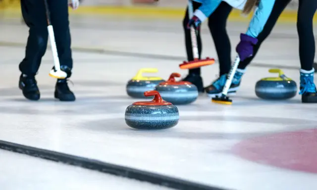 Curling ouders met hun stenen op het ijs. De spelers buigen zich voorover, klaar om te gooien.